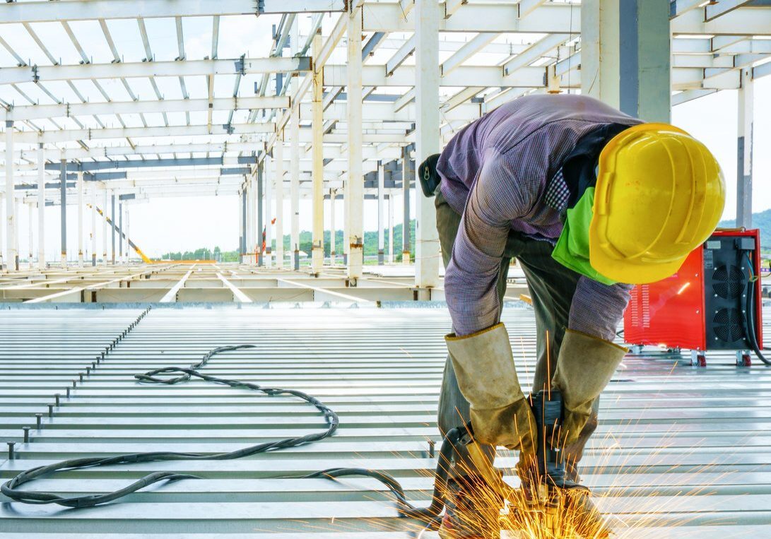 Welder are welds re-bar shear keys metal deck slab of mezzanine floor under the construction building in the factory with blue sky